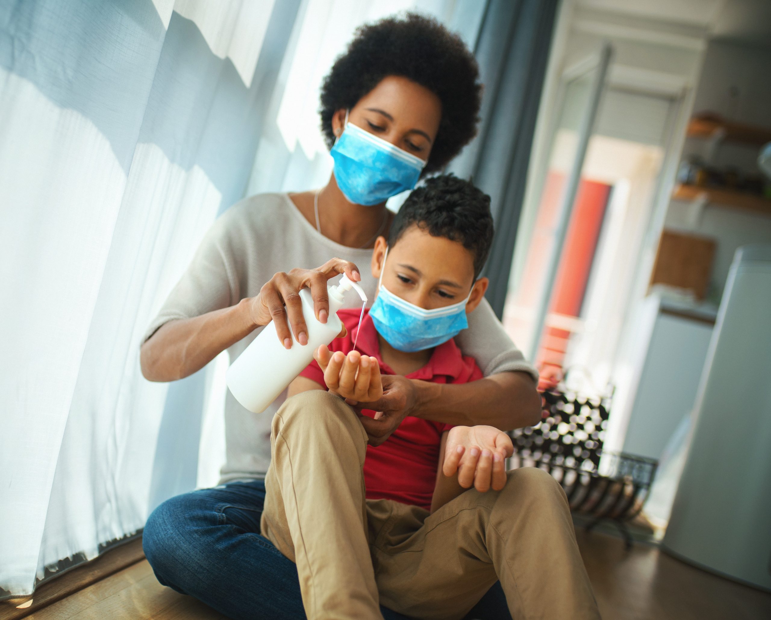 Mother and child wearing face coverings apply hand sanitizer